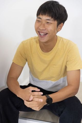Smiling asian man wearing metal braces and smartwatch, sitting in minimalist interior