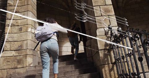 Walking two teens ascending historic stone steps under arched entrance with backpacks