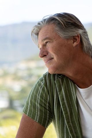 Mature man gazing through window at coastal skyline contemplative relaxed lifestyle portrait
