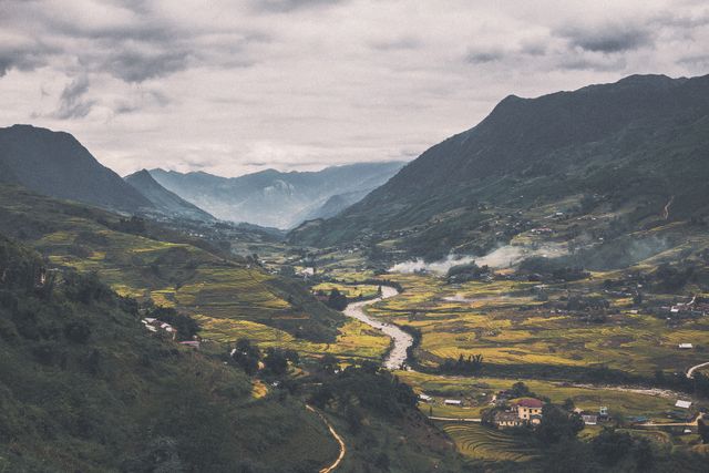 Beautiful scenic view capturing a mountainous valley with a winding river, enveloped with lush green rice terraces. Mist covers distant mountains, enhancing the tranquil atmosphere. Perfect for travel blogs, nature poster, and countryside-themed promotions.