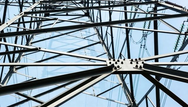 Geometric steel transmission tower lattice converging at bolted joint with power lines
