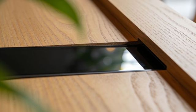 Glossy black recessed inlay reflecting green leaves on oak grain tabletop close-up