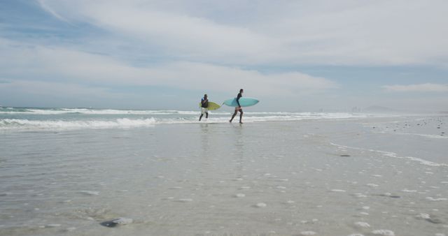 African american father and teenage son walking on a beach holding surfboards and talking. healthy outdoor family leisure time together.