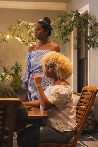 Women conversing in cozy dining nook with string lights and indoor plants