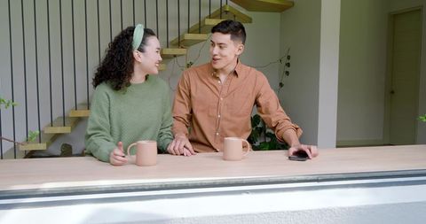 Couple Smiling at Breakfast Bar with Mugs and Smartphone