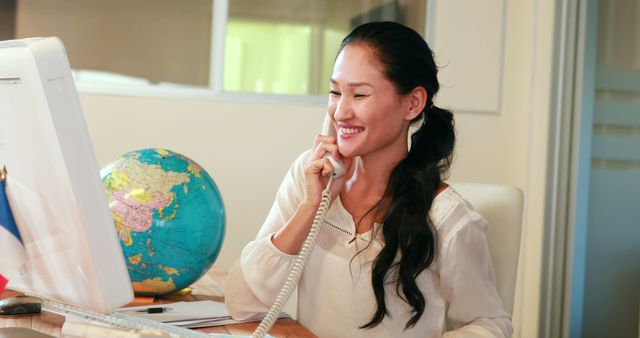 Smiling Woman Talking on Landline Phone in Office with Globe on Desk - Download Free Stock Images Pikwizard.com