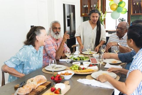 Multigenerational friends sharing joyful kitchen meal with wine, charcuterie, fruit and balloons