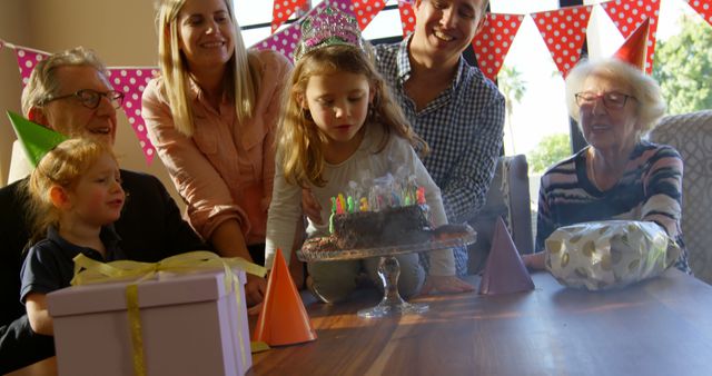 Family celebrating young girl's birthday with cake and presents, including elders, parents, and siblings. Ideal for articles or ads about family events, birthday parties, togetherness, and traditions.
