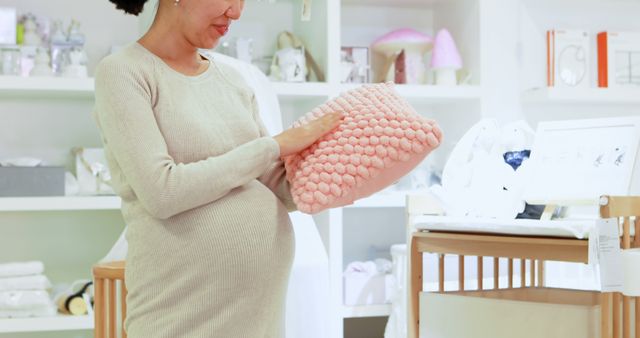 This image depicts a pregnant woman shopping for baby items in a specialty store. She is holding a pink blanket, possibly considering it for her upcoming baby. The background features various baby products and furniture, suggesting an environment catered to expecting parents. This image can be used in articles about pregnancy, retail ads for baby stores, maternity magazines, and blogs on preparing for a newborn.