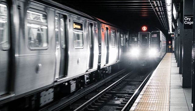Motion blur stainless-steel subway train approaching underground platform with headlights