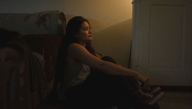 Contemplative woman sitting on floor leaning against bed in warm lamp light at night