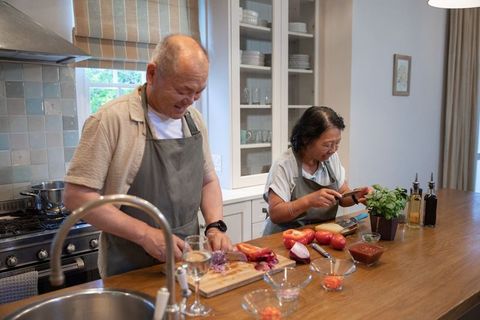 Asian senior couple cooking at kitchen island chopping vegetables sharing joyful moment