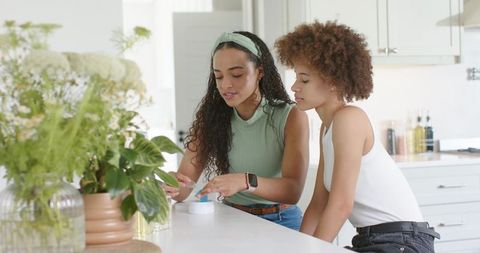 Young african american women applying skincare at sunlit kitchen island with potted plants