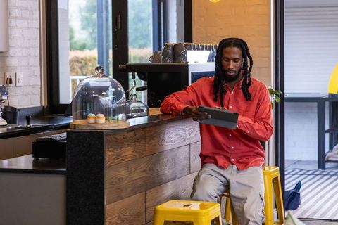 African american man using tablet at cozy cafe counter, cupcakes on display, espresso