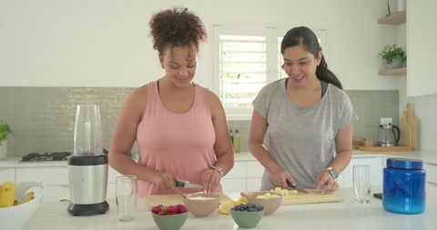 Friends preparing smoothie together at bright modern kitchen island