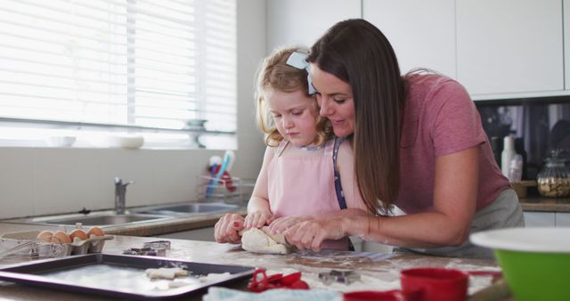 Mother and young daughter baking together in home kitchen, cultivating skills, spending quality family time. Ideal for use in parenting blogs, culinary websites, family-oriented products advertising, educational material.