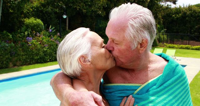 Elderly couple kissing and embracing by poolside, representing love and affection in old age. Useful for topics on romance, retirement lifestyle, summer relaxation, senior relationships, and intimacy.