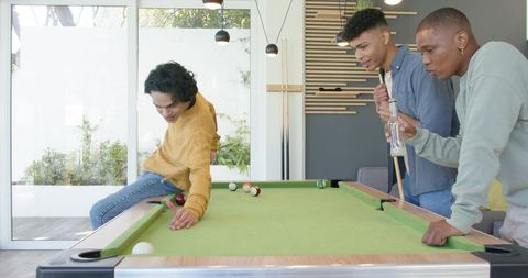 Three friends playing pool in modern game room with natural light, casual hangout