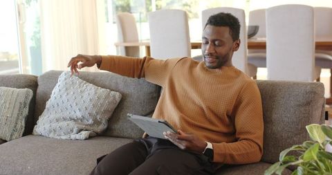 African american man relaxing on sofa with tablet and textured pillows in bright living room