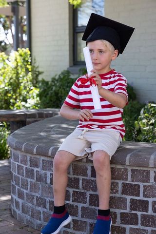Preschool graduation boy wearing mortarboard holding diploma sitting on brick ledge