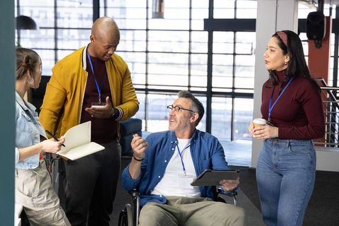 Diverse team collaborating in modern office with wheelchair user leading discussion