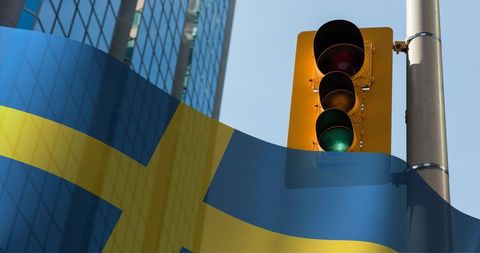 Green traffic signal glowing over swedish flag overlay on sunlit glass highrise