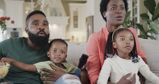 African American family of four enjoying TV time together in a cozy living room. Perfect for advertising family-oriented products, promoting home entertainment services, or illustrating articles on family values and bonding. Suitable for blogs, social media posts, or family-related website content.