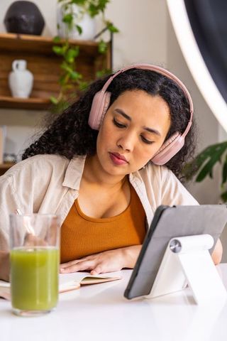 African american woman wearing pink headphones studying with tablet and notebook