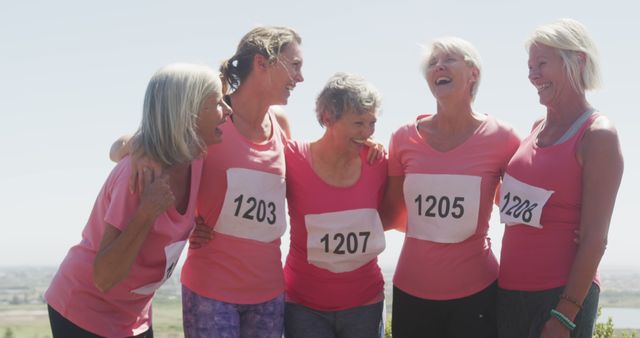 Happy diverse women wearing pinkt t-shirts with numbers embracing and smiling. Sport, support, friendship, healthy and active lifestyle.