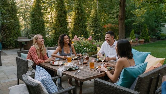 Friends enjoying casual summer backyard dinner party around wooden table