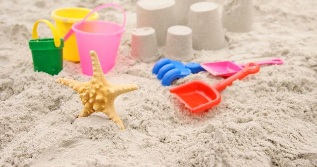 Colorful sand toys including buckets, shovels, and a starfish on sandy beach. Sandcastles in the background. Ideal for promoting family vacations, kids' activities, summer fun, and seaside adventures.