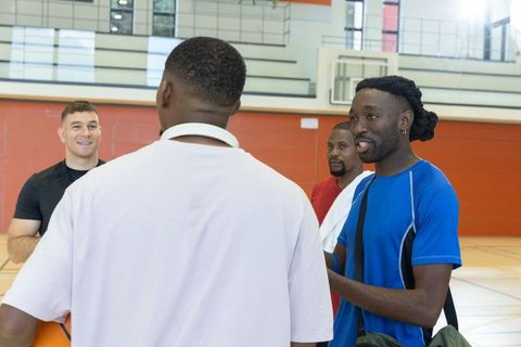 Men's basketball teammates talking on indoor court holding basketball and gym bags