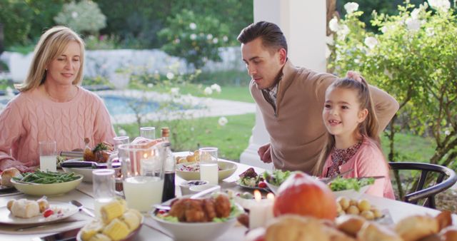 Family of three gathers around table full of delicious foods in outdoor garden. Scene suggests warmth, unity, and enjoyment of good food. Can be used for themes of family bonding, holiday celebrations, or outdoor dining. Perfect for advertisements, brochures, and social media promotions related to family lifestyle, gardening, and holidays.