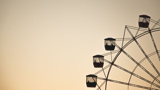 Ferris wheel casting a striking silhouette against soft, warm colors of sunset sky, evoking a serene, peaceful evening at the amusement park. Perfect for travel blogs, vacation websites, and promotional material for theme parks. Ideal for conveying themes of relaxation, leisure, and nostalgia.
