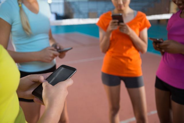 This image shows female volleyball players standing on a court, using their mobile phones. Ideal for illustrating themes of technology in sports, team communication, and the integration of digital devices in active lifestyles. Useful for articles, blogs, or advertisements related to sports, fitness, technology, and social media.