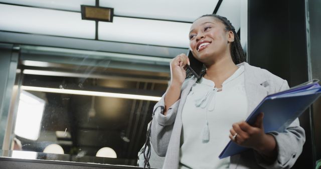 Happy african american casual businesswoman talking on smartphone in office elevator. Casual office, business, communication and work, unaltered.