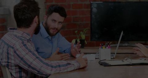 Bearded Manager Leading Team Meeting in Modern Brick-Office Workspace with Laptop and Monitor