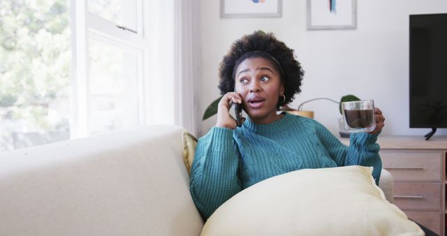 Middle-aged woman lounging on a comfortable sofa at home, holding a cup of tea and engaging in a phone conversation. Perfect for promoting home lifestyle, comfort, leisure activities, modern communication, and indoor living themes.