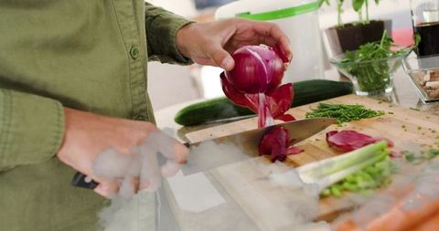 Sunlit home cooking: woman preparing red onion and fresh herbs on wooden cutting board