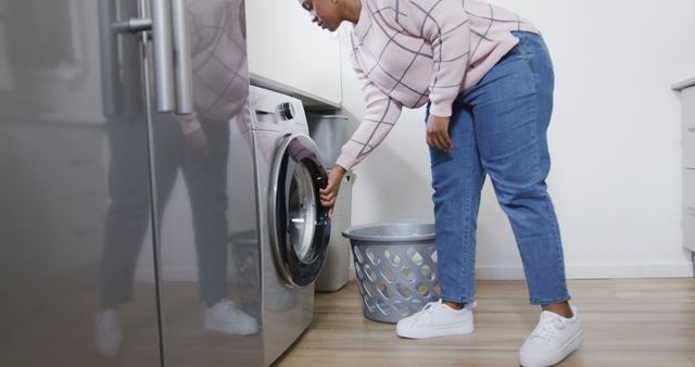 Woman placing clothes into front-loading washing machine. Ideal for content on household chores, modern living, home appliances, and daily domestic routines. Can be used in articles about laundry tips, home maintenance, or cleaning habits.