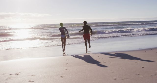 African american couple running with surfboards on the beach. holiday and healthy outdoor leisure time by the sea.