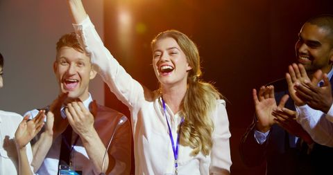 Joyful businesswoman cheering on stage in seminar audience applauding