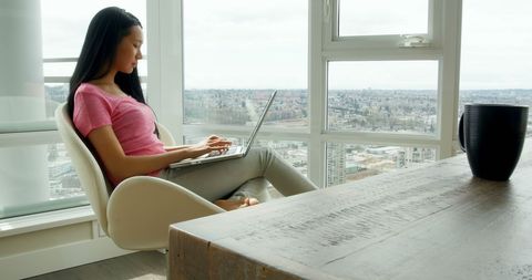 Woman working remotely on laptop near large window