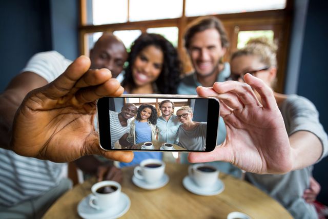 Group of friends taking a selfie in a cafe, enjoying coffee and each other's company. Perfect for use in advertisements, social media posts, and articles about friendship, socializing, and modern lifestyle.