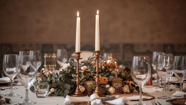 Warm brass candlelight centerpiece featuring eucalyptus garland and cream roses for elegant dining