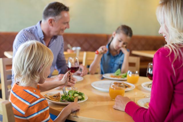 Family enjoying a meal together at a restaurant. Parents and children are sitting around a table, eating and drinking. This image can be used for advertisements, family-oriented content, restaurant promotions, and lifestyle articles.