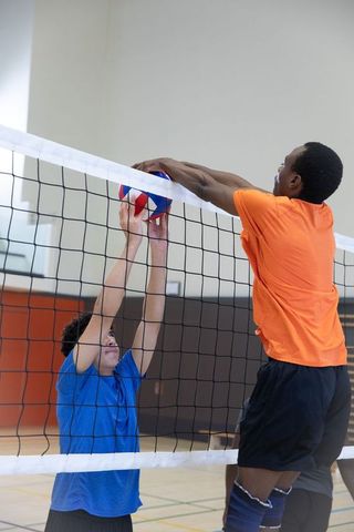 Teen volleyball players jumping and contesting block at indoor gymnasium net