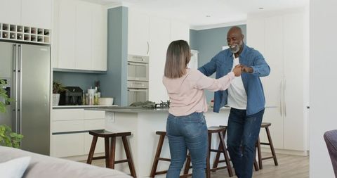 Mature african american couple dancing in bright modern kitchen, joyful home moment