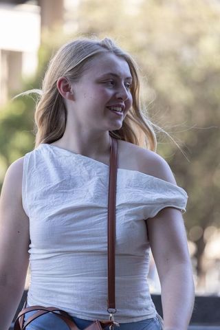 Smiling young woman standing in urban park wearing off-shoulder top and crossbody bag
