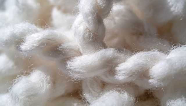 Thick off-white wool yarn macro showing braided ropes, soft fiber texture, knit twist
